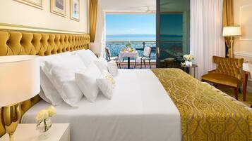 Habitación de hotel con una cama grande, un balcón con mesa y sillas, y vistas al mar.