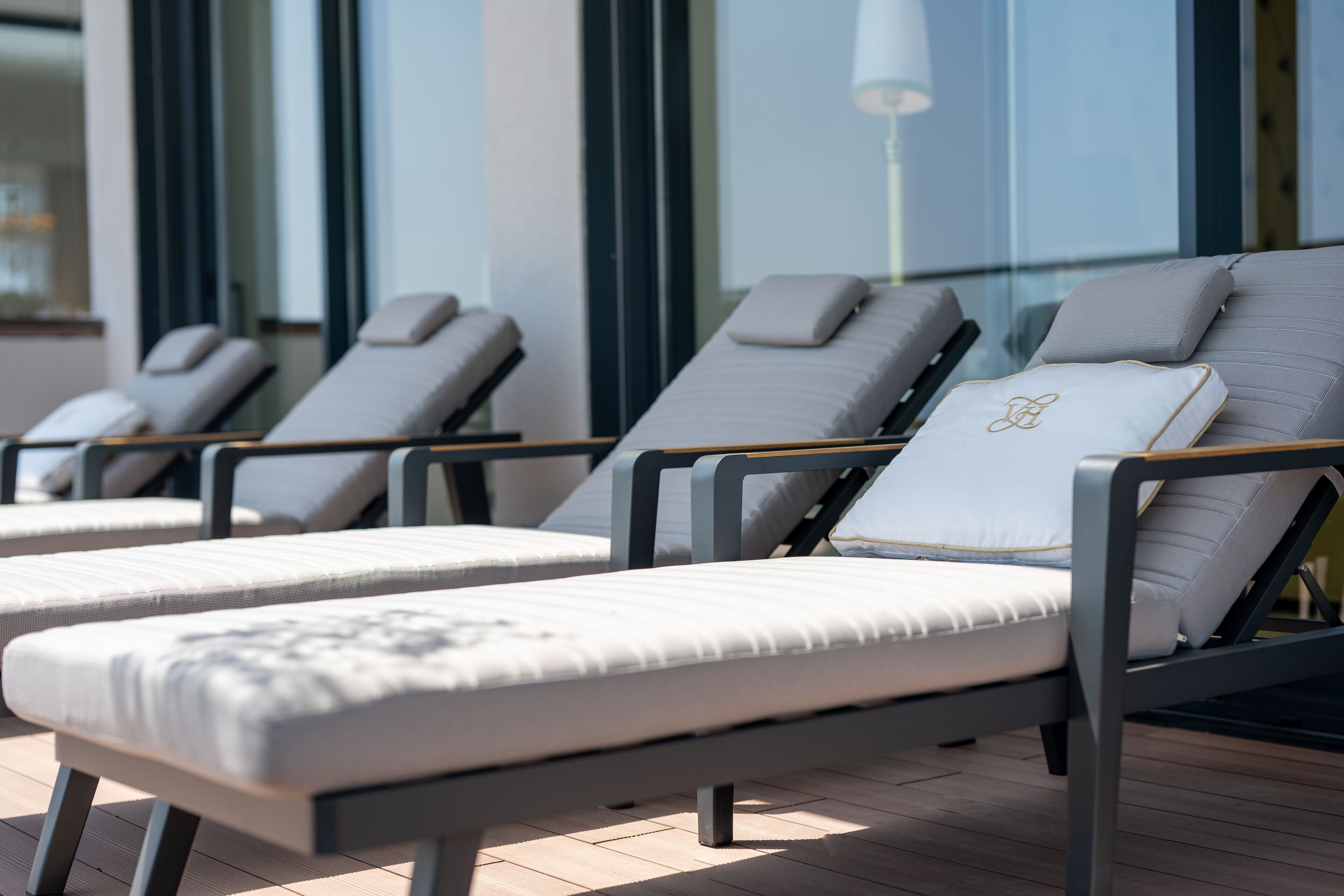 Una fila de tumbonas con almohadillas, ubicadas sobre una terraza de madera, probablemente perteneciente a un hotel o resort.