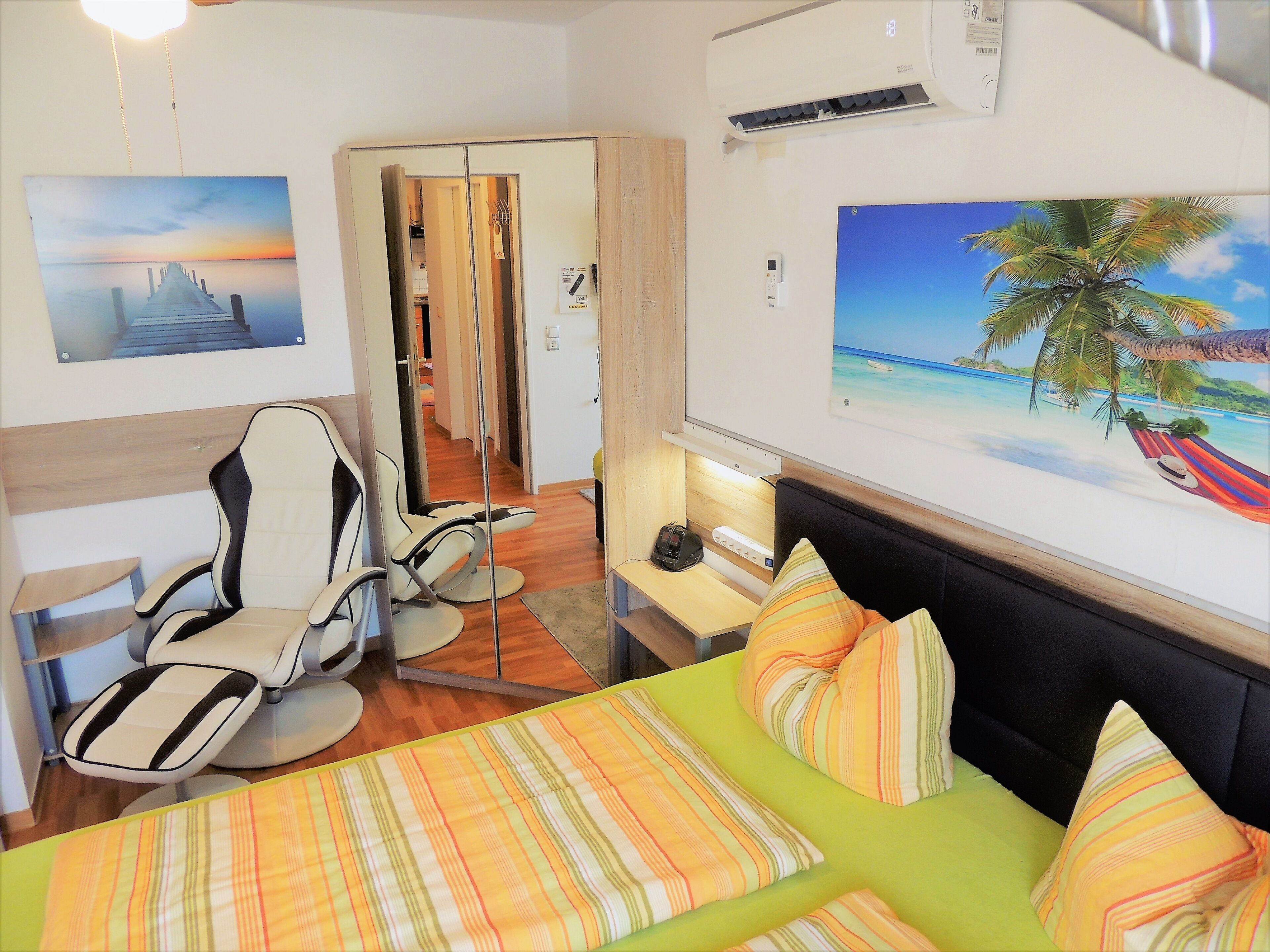 A hotel room with a bed, a chair, a desk, and a painting of a sunset.