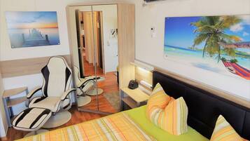 A hotel room with a bed, a chair, a desk, and a painting of a sunset.
