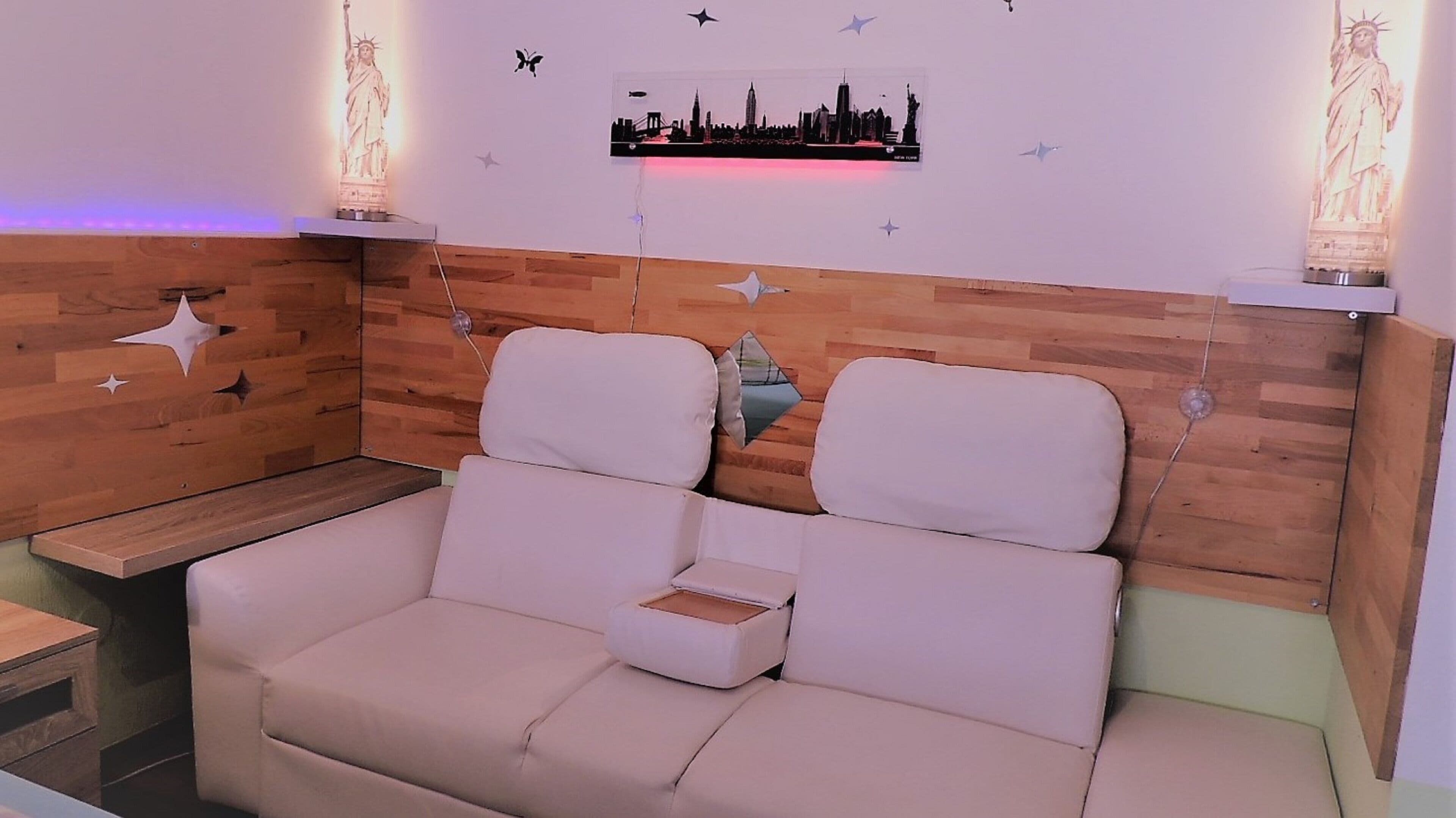 Ein modernes Zimmer mit einem Holzkopfschild, zwei weißen Sofas, einem kleinen Tisch und Wandkunst, darunter eine Stadtansicht und sternförmige Ausschnitte.