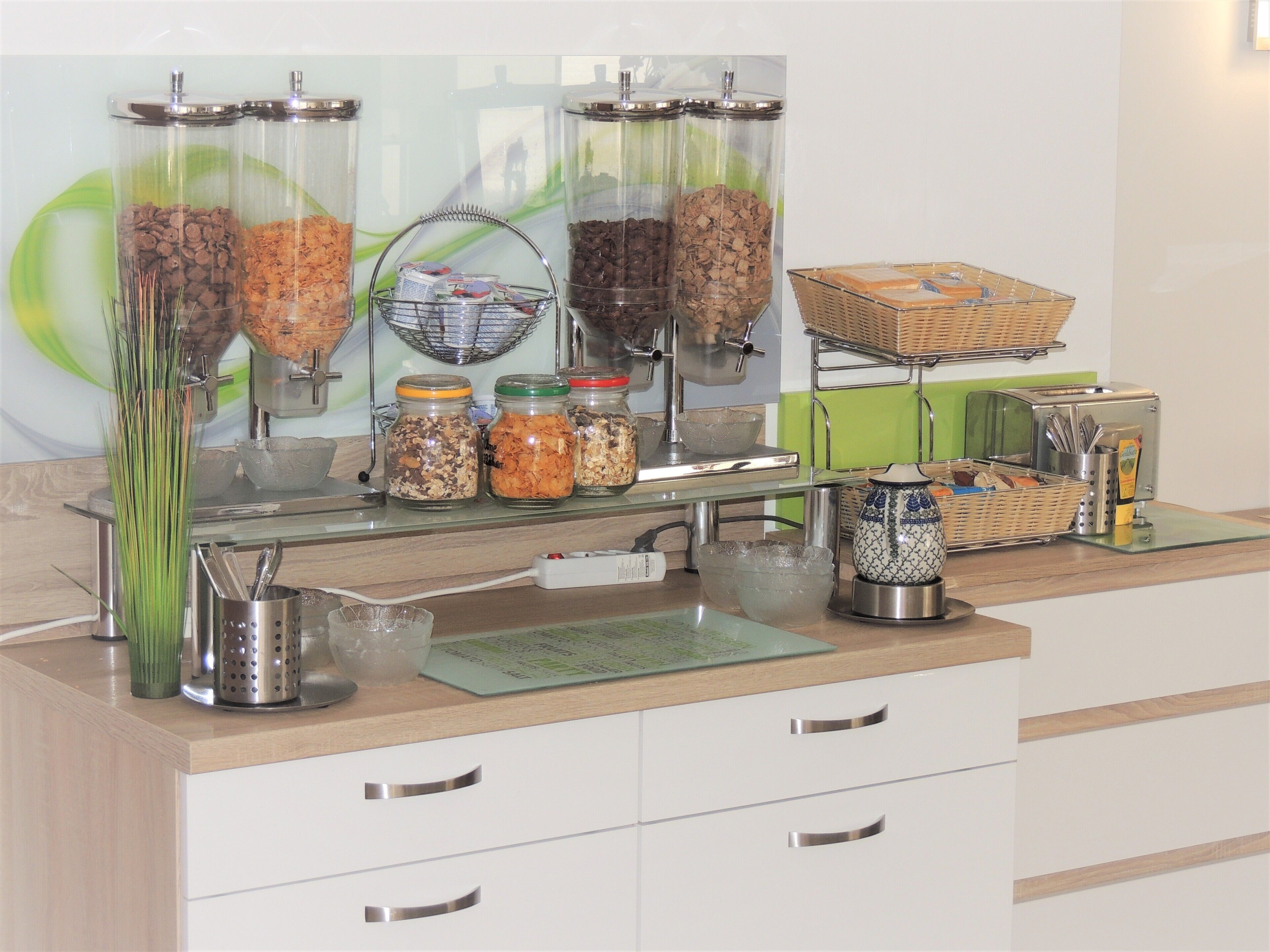 Een ontbijtbuffet met diverse soorten eten en toevoegingen, waaronder potten met ontbijtgranen, een koffieapparaat en een broodrooster.