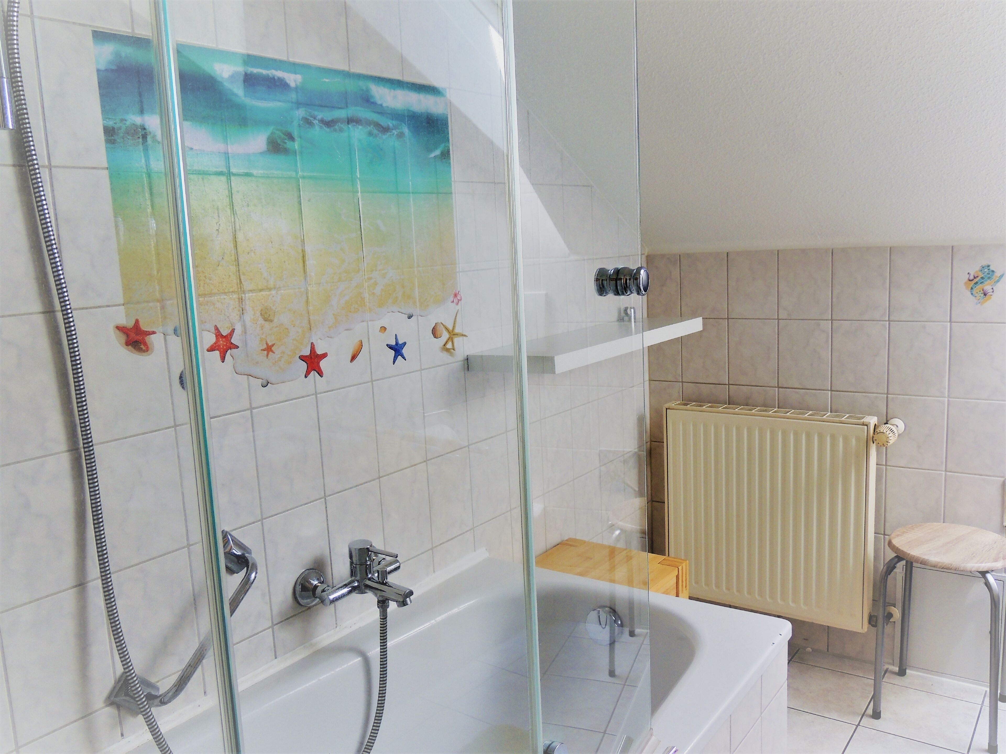 Une salle de bain avec une douche à parois de verre, une baignoire, un porte-serviettes et un radiateur.