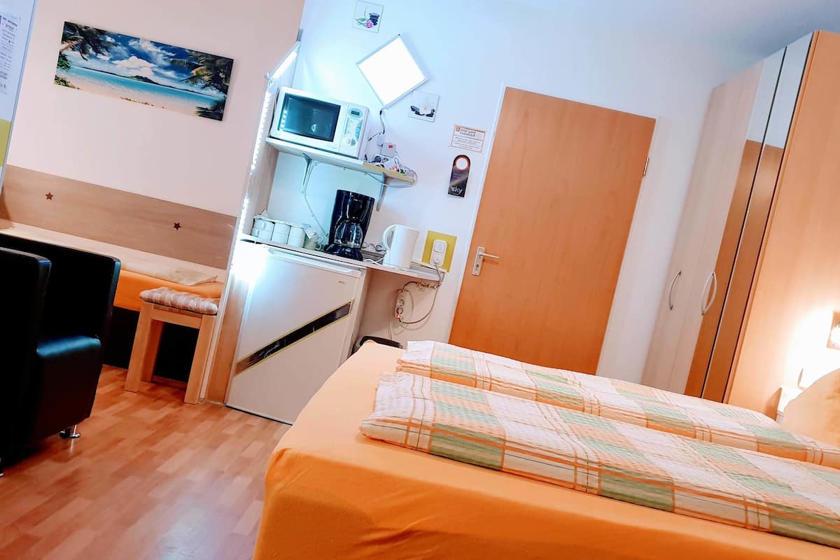 A compact hotel room with a bed, a small kitchenette, a desk, and a chair.