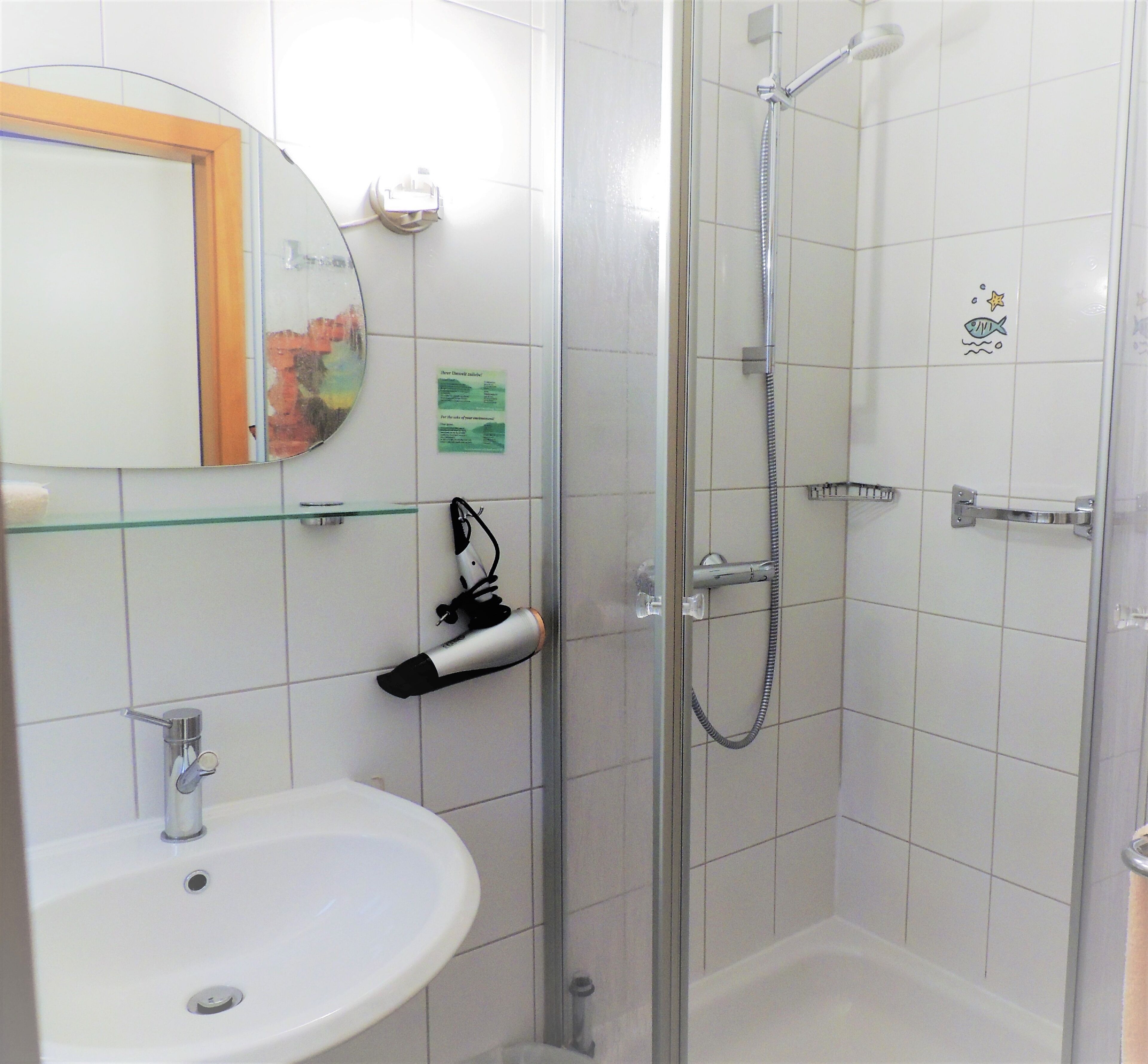 A bathroom with a glass shower enclosure, a white sink, and a mirror with a decorative frame.