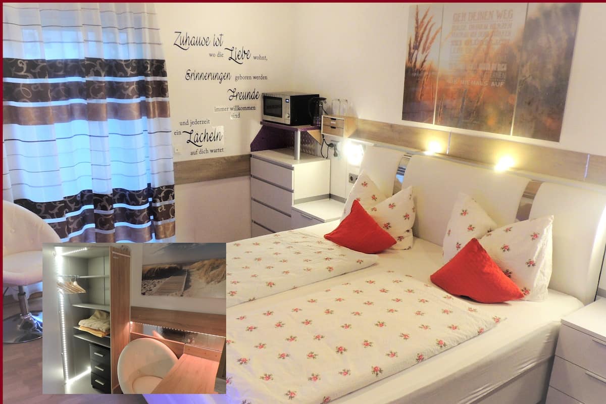A bedroom with a bed, bedside tables, a desk, and a chair. There is a wall with a poster and a curtain.