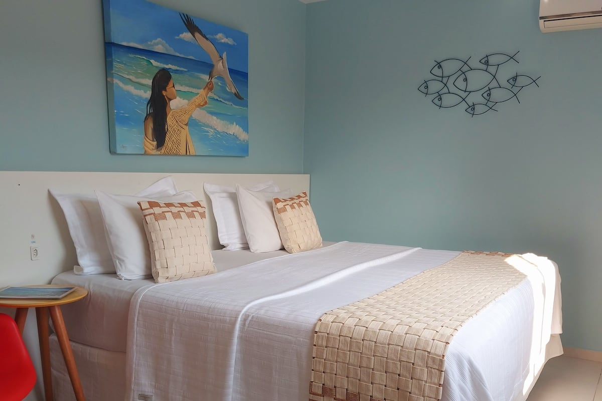 A bedroom with a bed, pillows, a small table, and a chair.