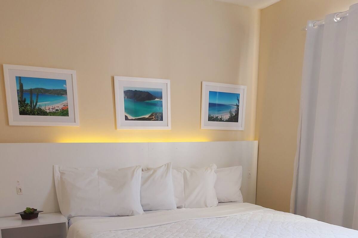 A neatly made bed with a white duvet, a nightstand with a small plant, and three framed pictures on the wall.