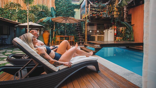 Zona de piscina con sillones, una terraza de madera y una pileta.