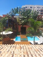 A pool area with a wooden deck, a hammock, and a view of a building in the background.