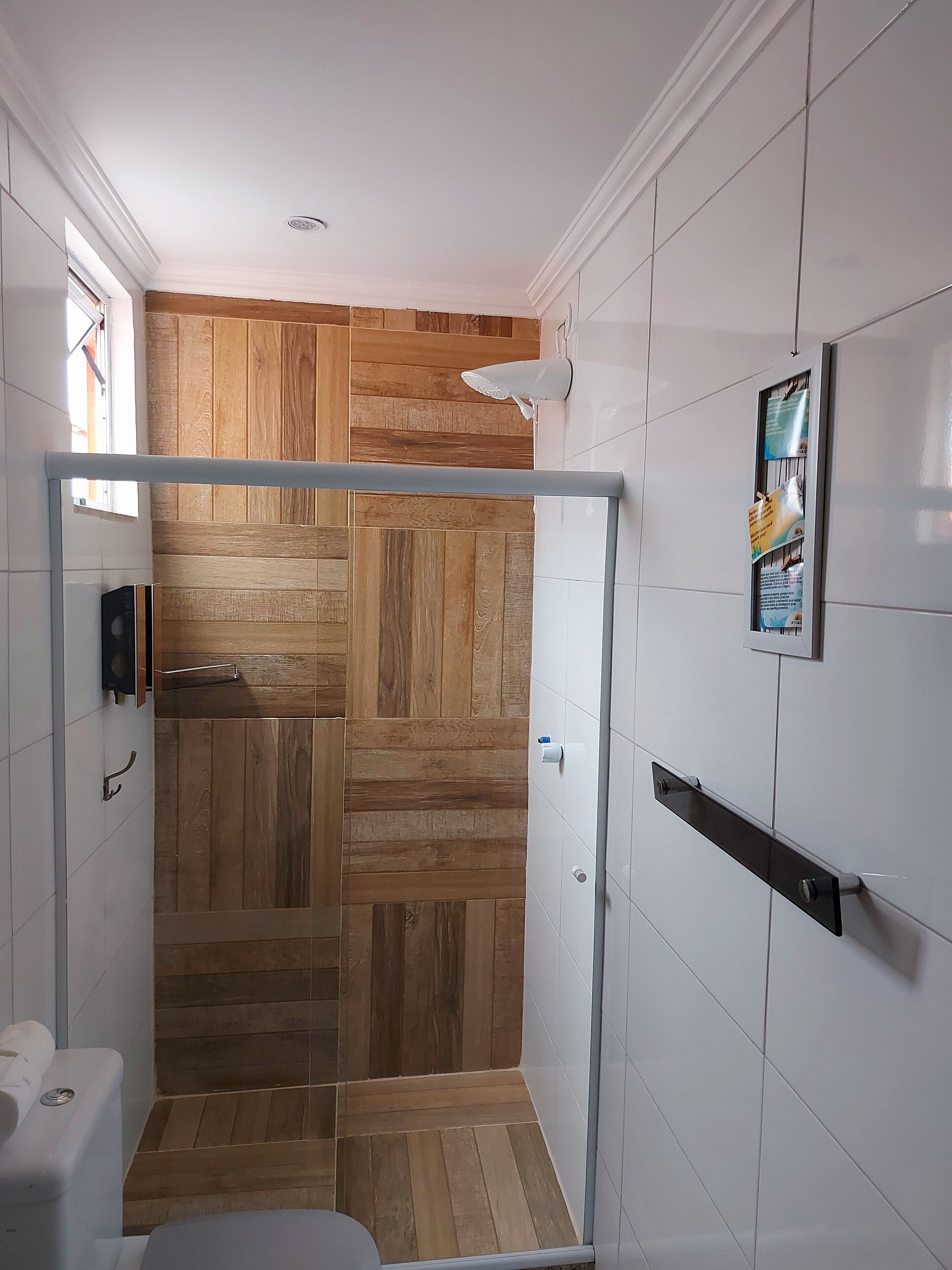 Un baño moderno con zona de ducha, pared de paneles de madera, azulejos blancos y puerta de cristal para la ducha.