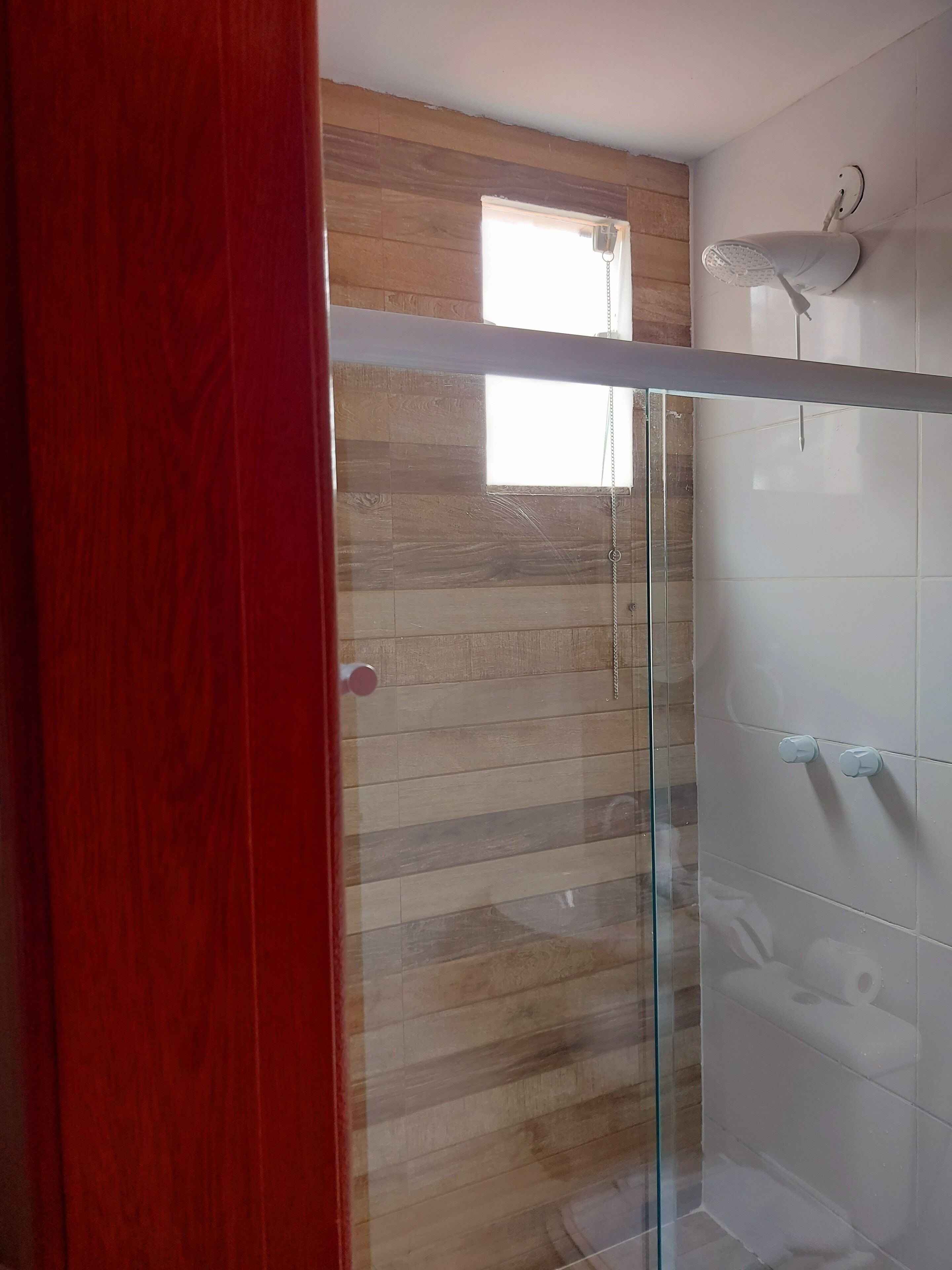 A glass-enclosed shower with a wooden wall and a white tiled wall.
