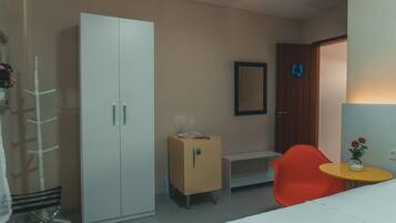 A room with a white wardrobe, a small cabinet, a mirror, a red chair, and a small table with a vase.