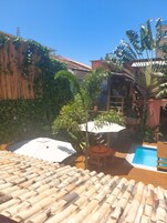 A rooftop with a swimming pool, surrounded by potted plants and a wooden pergola.