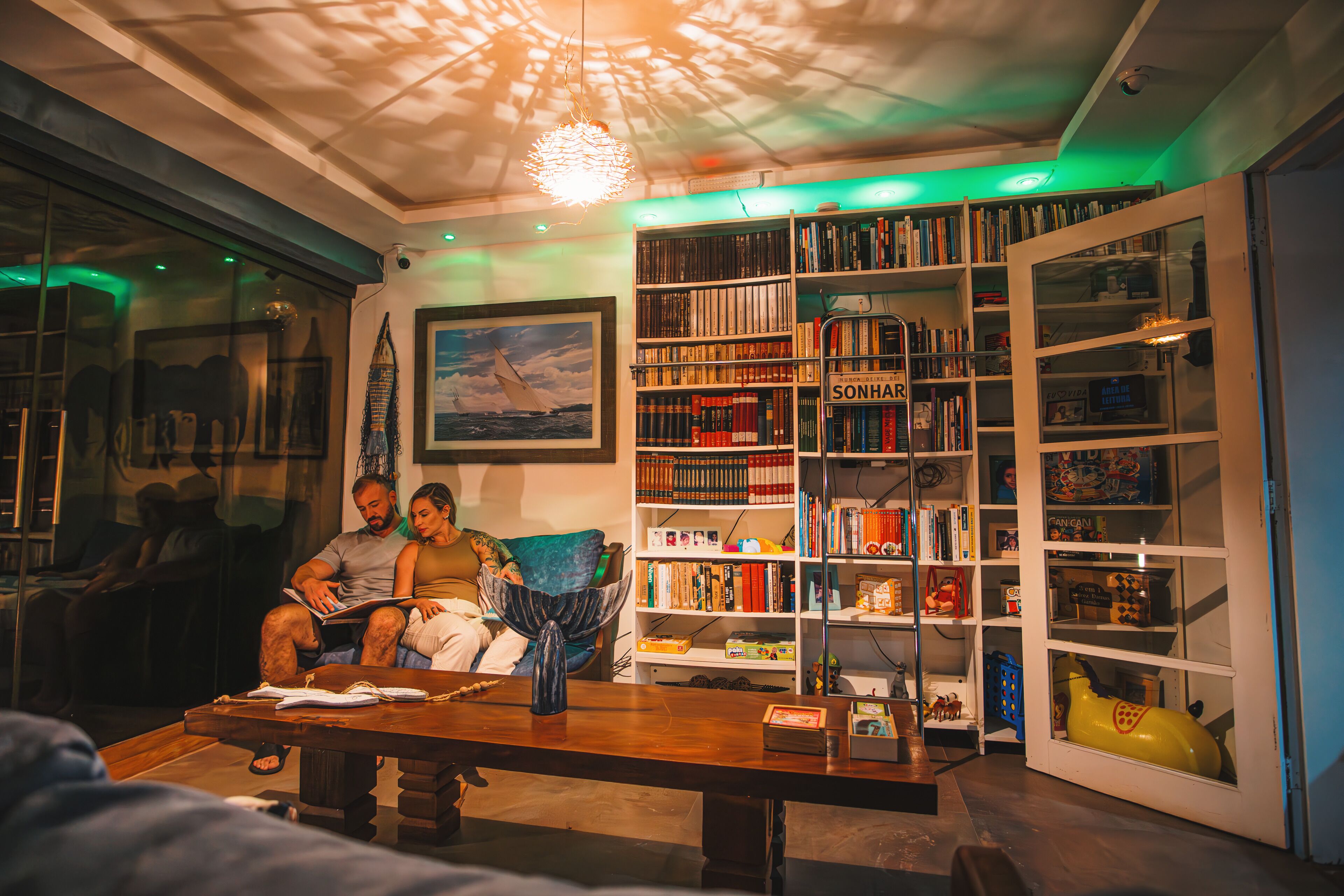 Una sala de estar acogedora con una amplia estantería, una mesa de comedor y una pareja leyendo.