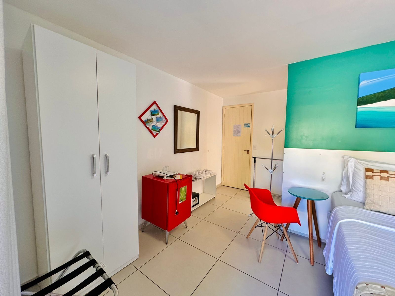 A hotel room with a bed, a desk, a red cabinet, and a chair.