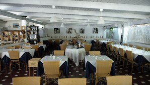 A restaurant with multiple tables and chairs, white tablecloths, and hanging pendant lights. - Baia dei Lombardi (Vieste)