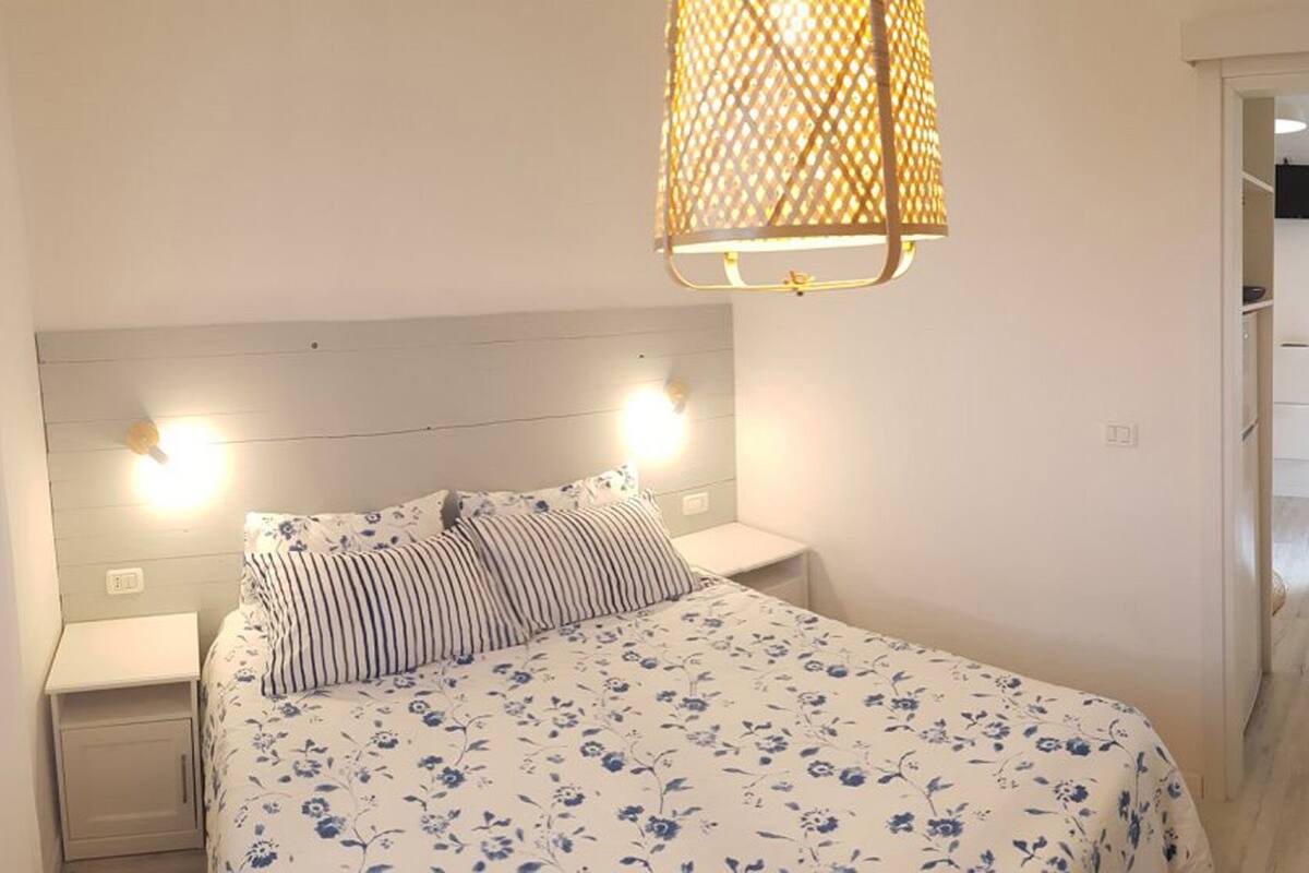 Un dormitorio con cama, dos mesitas de noche, lámpara colgante y puerta que da a un baño.
