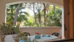 A dining area with a table set for two, overlooking a lush garden with various trees and plants. - Baia dei Lombardi (Vieste)