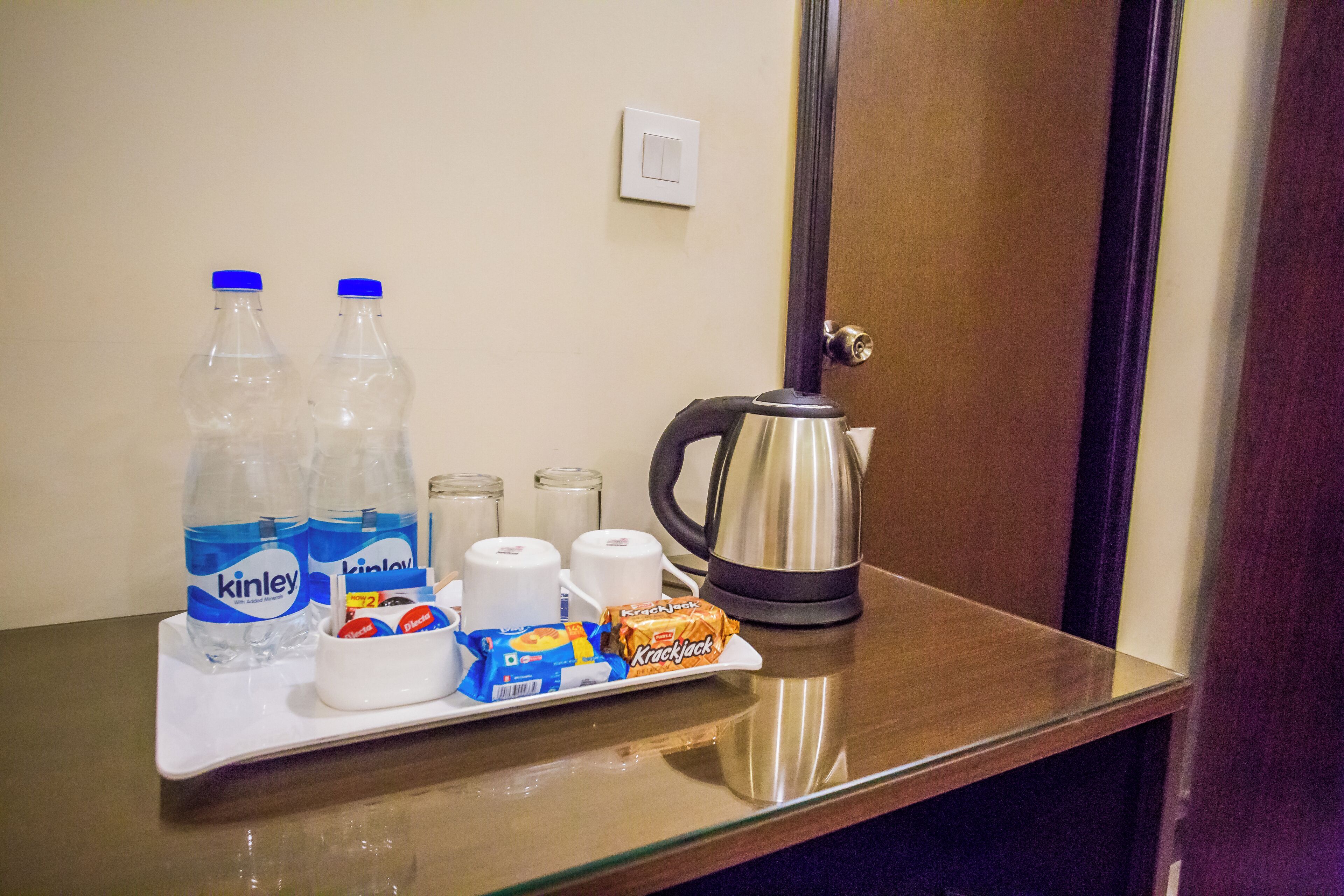 A hotel room's minibar with bottled water, coffee cups, a kettle, and snacks.