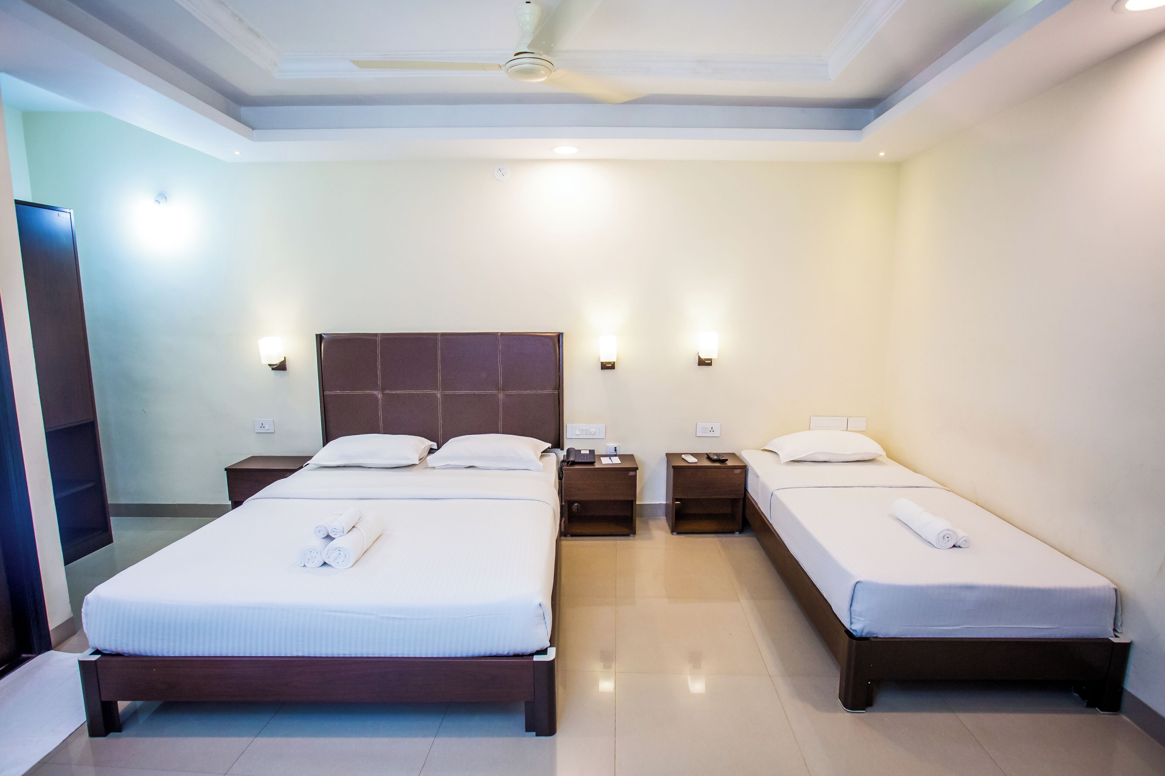 Habitación de hotel con dos camas individuales, una cama grande, un televisor de pantalla plana y un ventilador de techo.