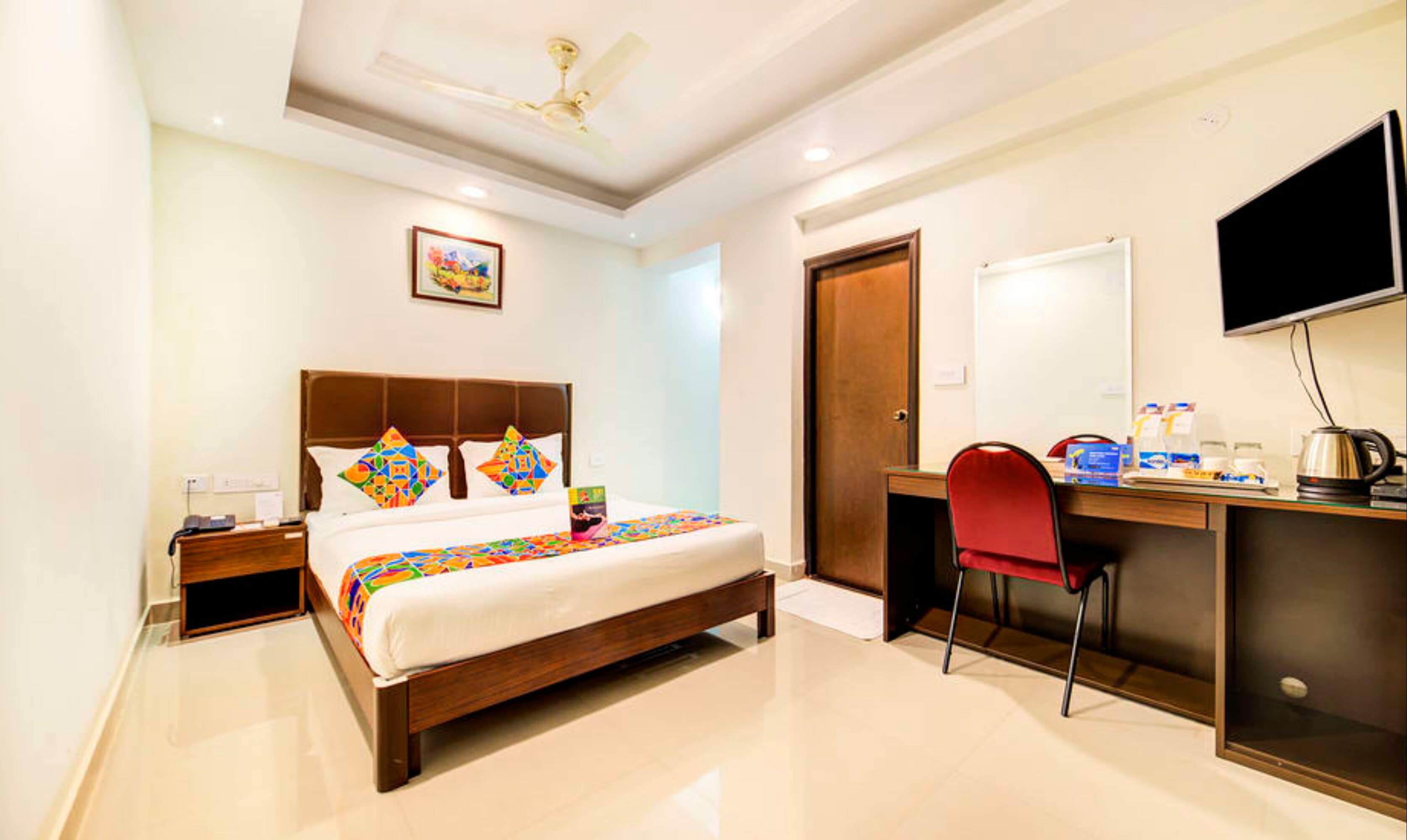 A hotel room with a bed, a desk, a chair, a television, and a ceiling fan.