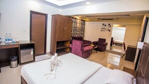 A hotel room with a bed, a desk with a trash bin, a wardrobe, a seating area with a chair, and a small table. - Hotel Menino Executive (Ponda)