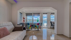 Un salon spacieux avec un canapé, des fauteuils aux couleurs vives et une vue sur la mer grâce à de grandes fenêtres.