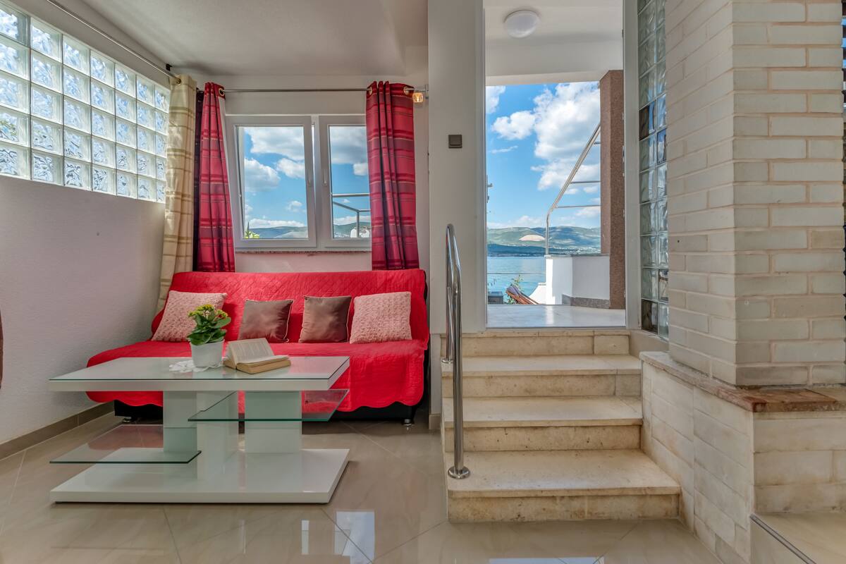 A modern room with a red sofa, a glass coffee table, and a view of the sea through large windows.