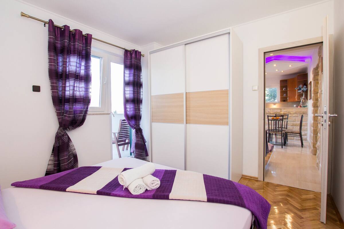 A hotel room with a bed, curtains, a wardrobe, and a view into the kitchen area.