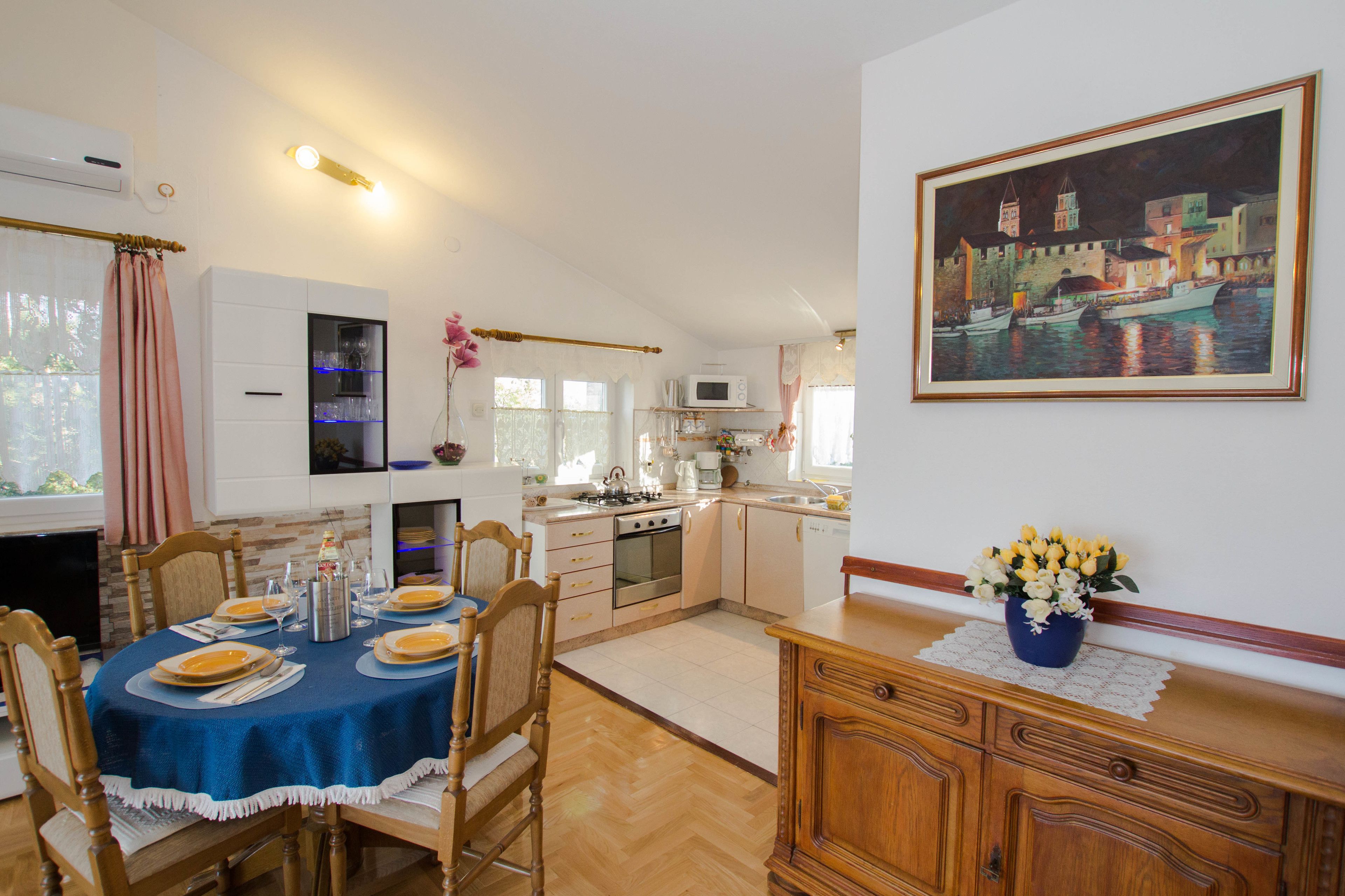 Een eetgedeelte met een tafel voor vier personen, een keuken met moderne apparatuur en een schilderij van een havenzicht aan de muur.