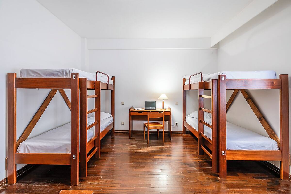 A room with four wooden bunk beds, a desk with a laptop, and a chair.