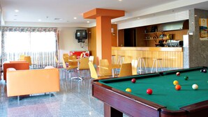 A pool table with balls, a bar area, and several chairs in a room with a tiled floor. - HI Foz Côa - Pousada de Juventude - Hostel (Vila Nova de Foz Coa)