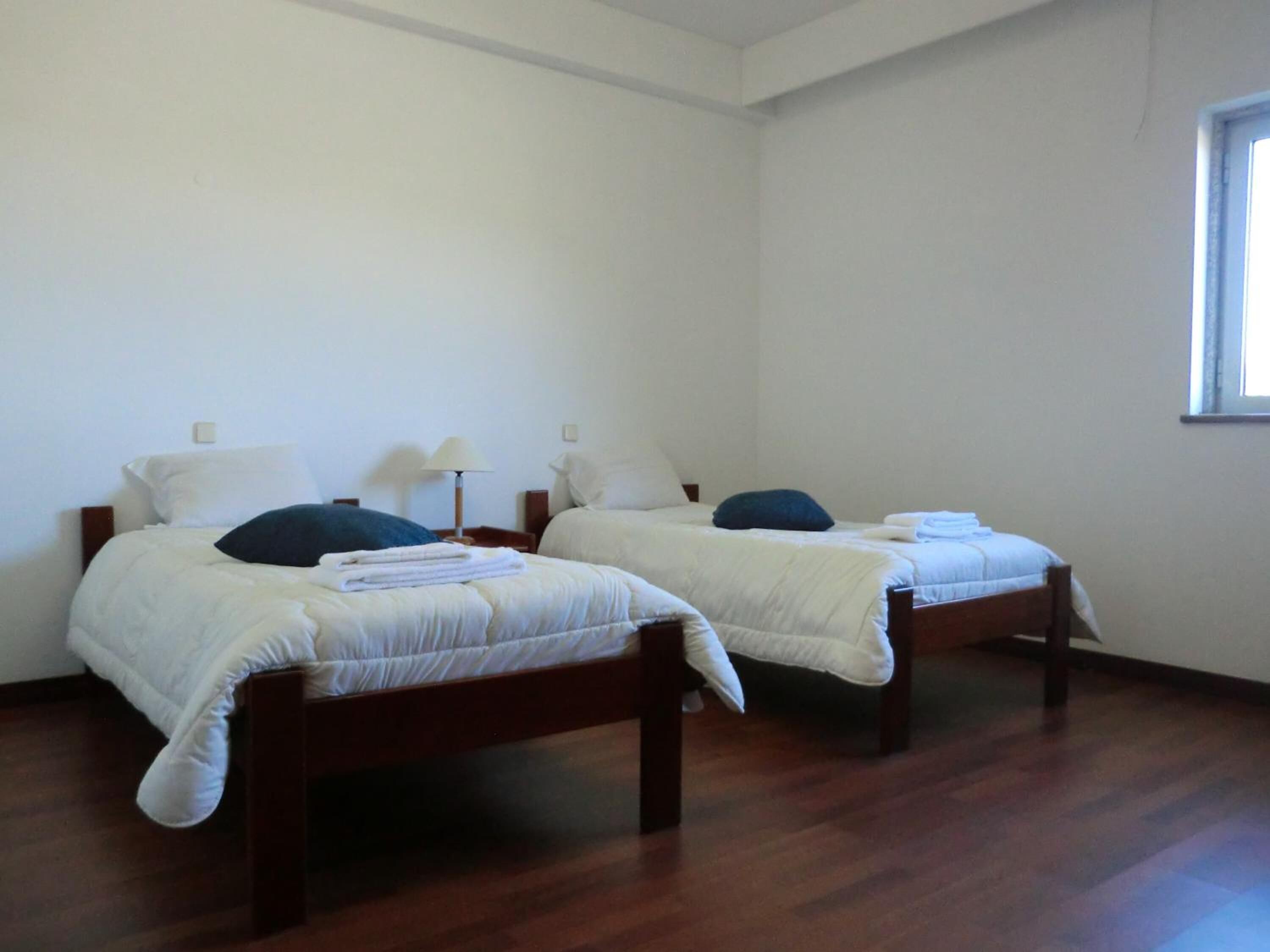 A room with two single beds, wooden headboards, white bedding, and a window on the right wall.