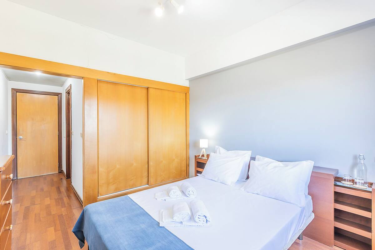 A hotel room with a bed, wooden wardrobe, and a nightstand with a lamp.