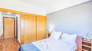 A hotel room with a bed, wooden wardrobe, and a nightstand with a lamp.