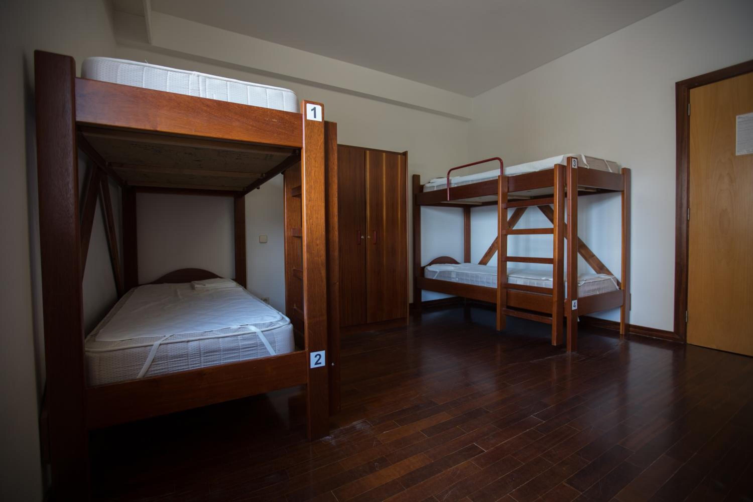 Ein Zimmer mit zwei Etagenbetten, Holzboden und einer Tür.