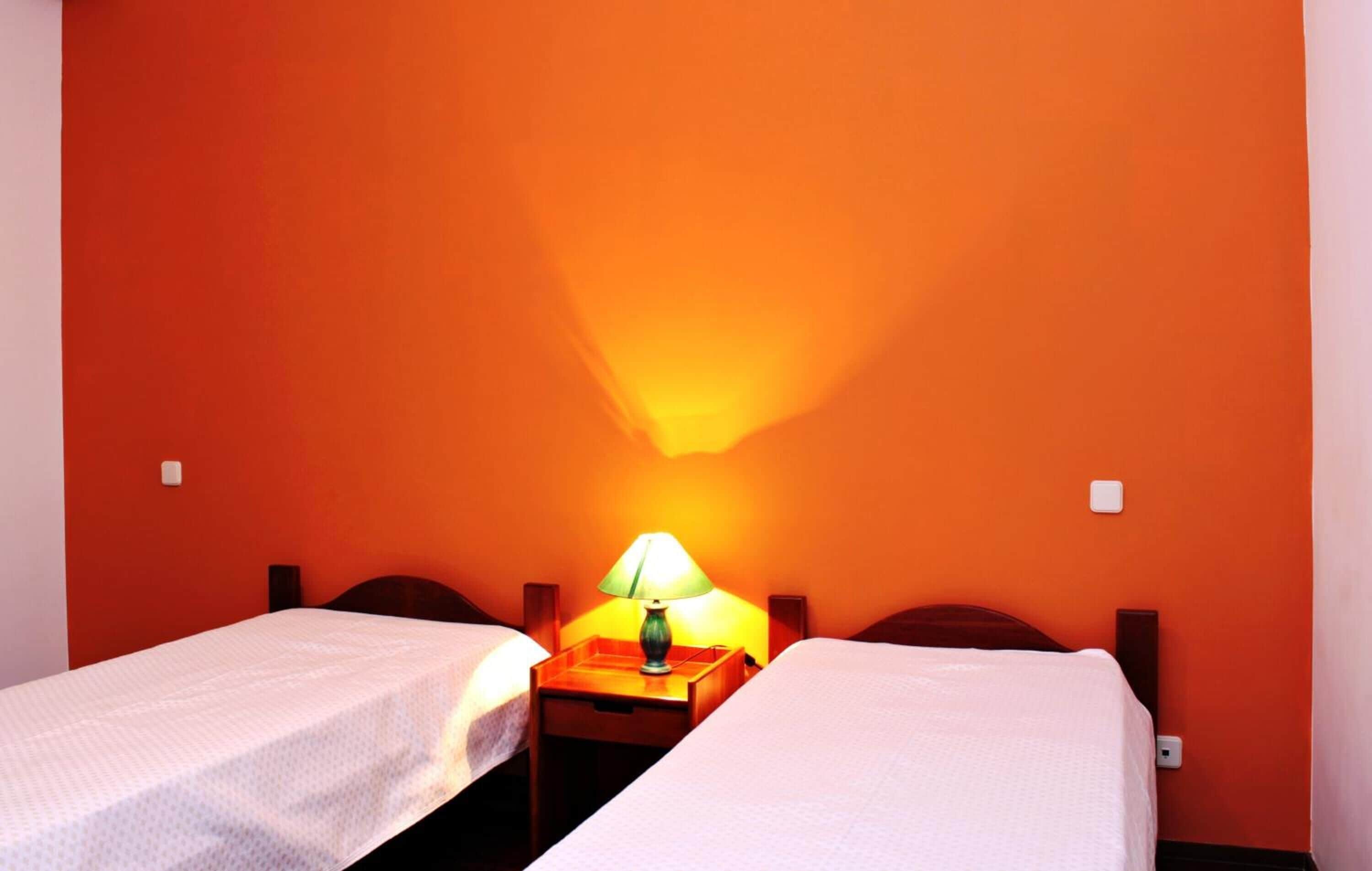 Une chambre avec deux lits simples, une table de chevet avec une lampe et des murs de couleur orange.