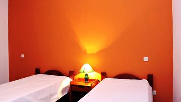 Une chambre avec deux lits simples, une table de chevet avec une lampe et des murs de couleur orange.