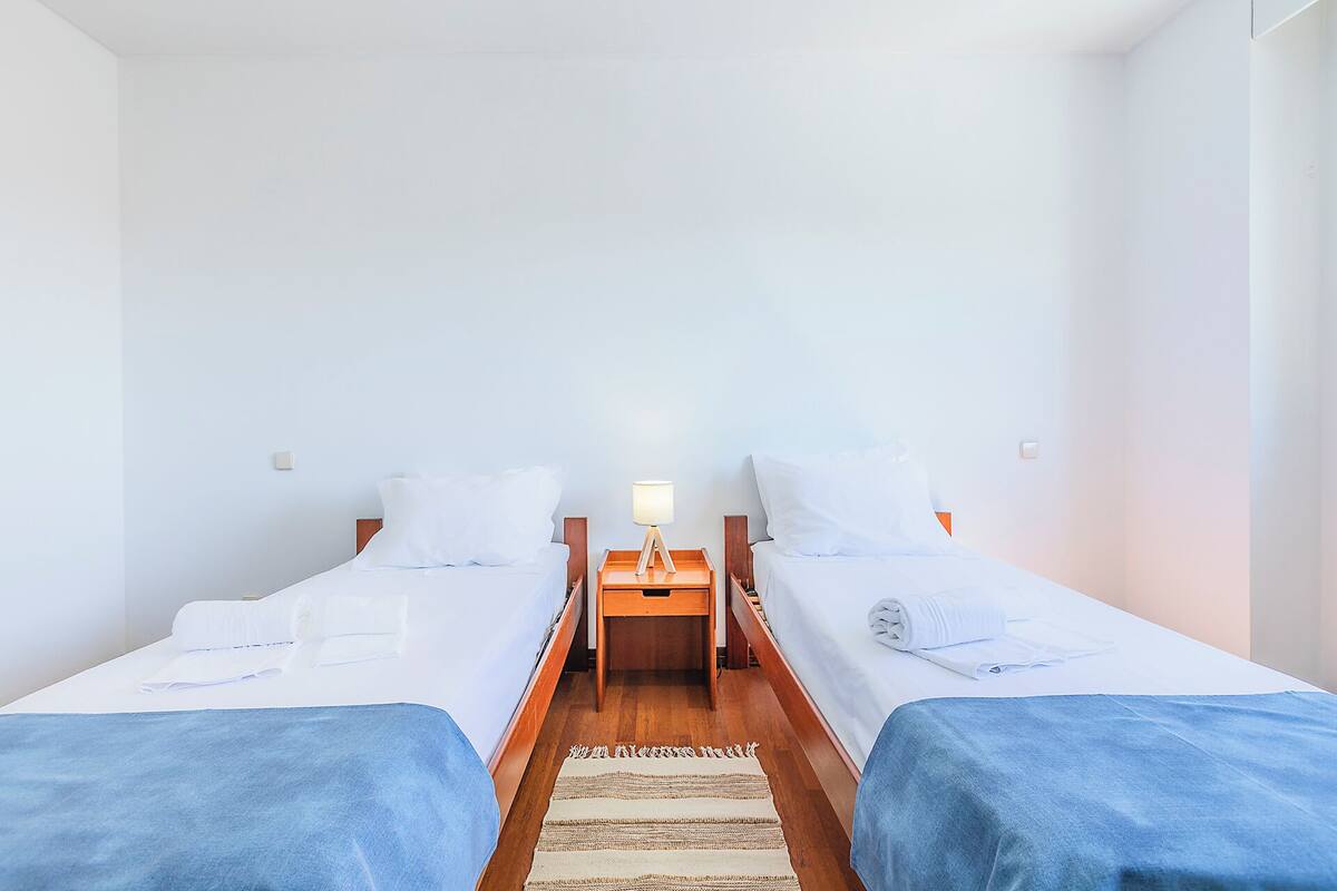 A twin room with two beds, a nightstand with a lamp, and a wooden floor.