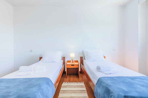 A twin room with two beds, a nightstand with a lamp, and a wooden floor.