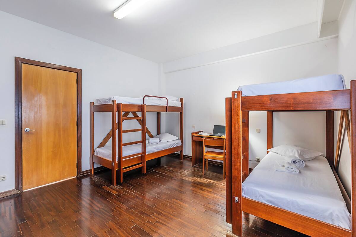 A room with three wooden bunk beds, a desk with a laptop, and a door.