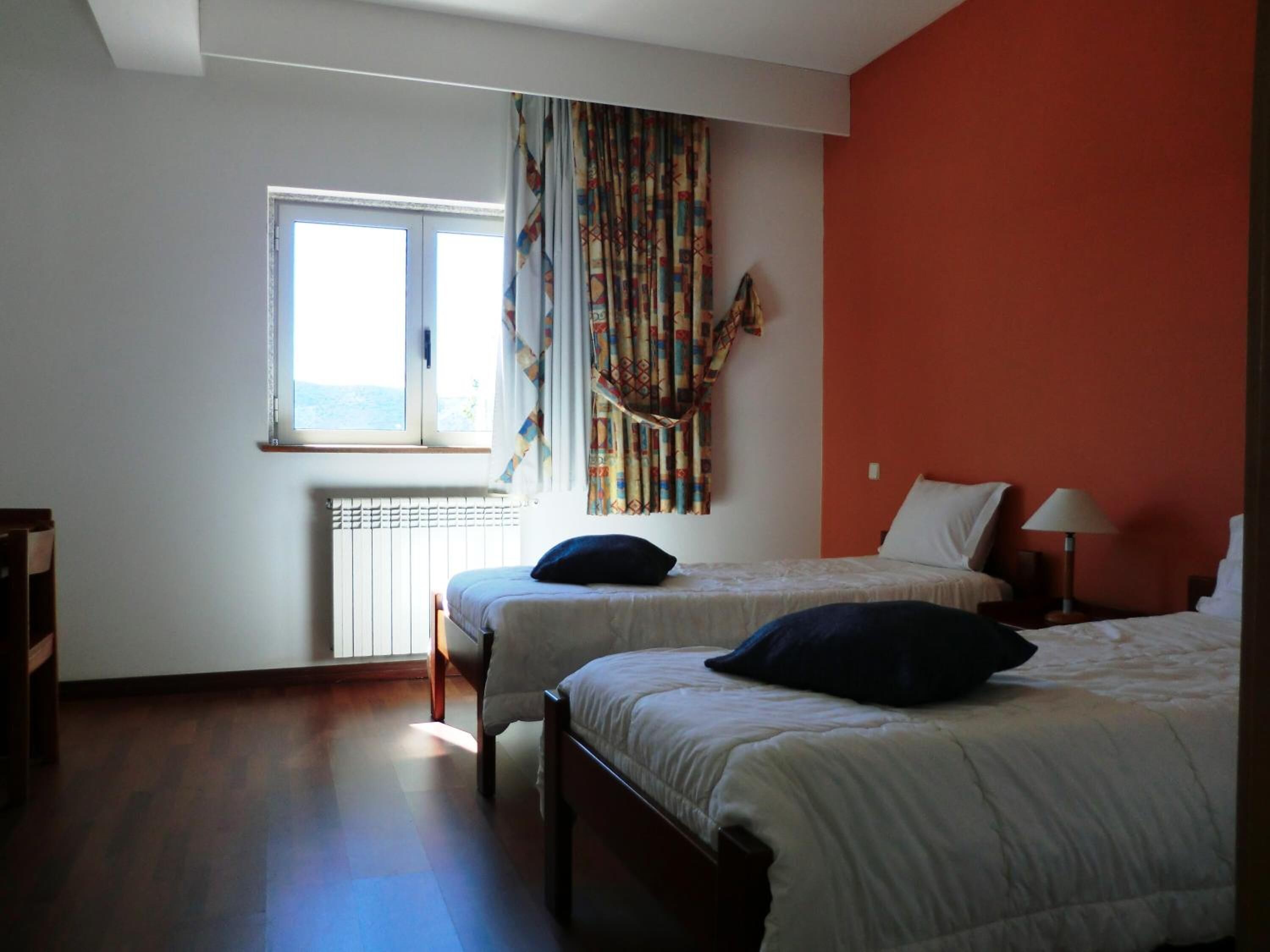 Une chambre avec deux lits, une fenêtre, un radiateur et un rideau.