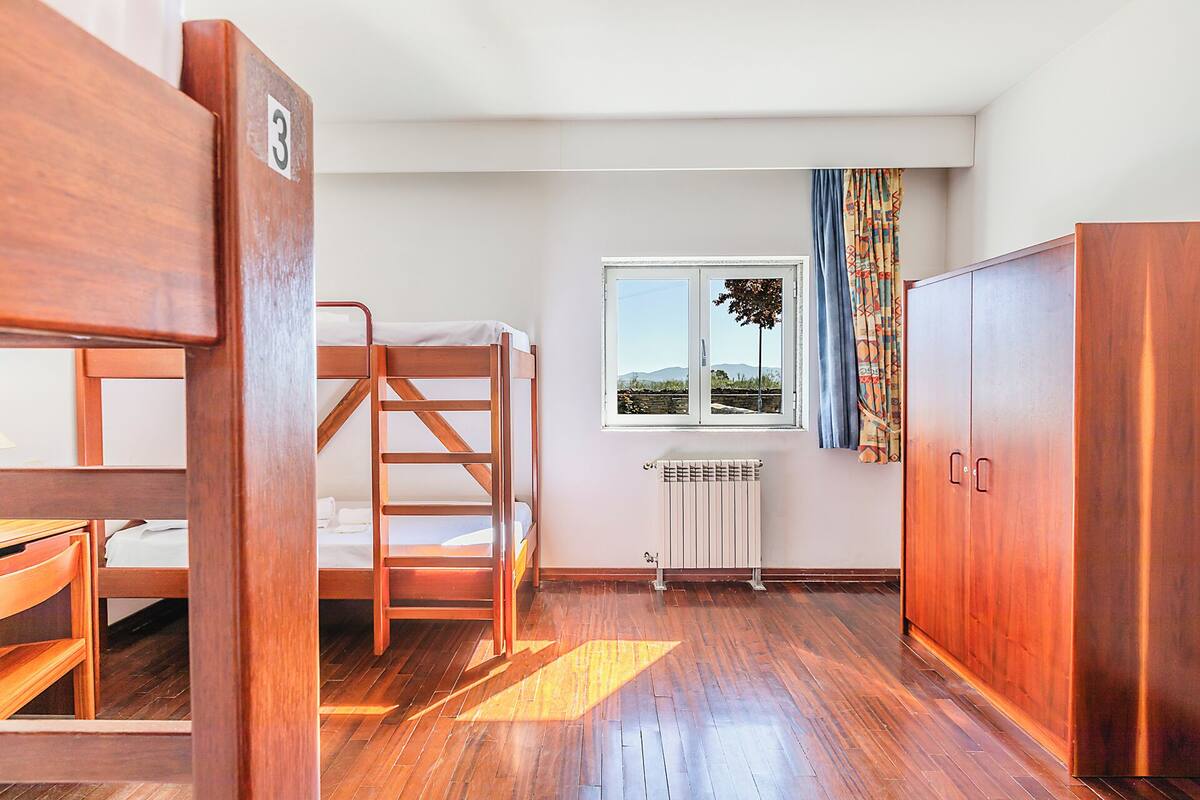 A room with a bunk bed, a radiator, a wardrobe, and a window with a view.