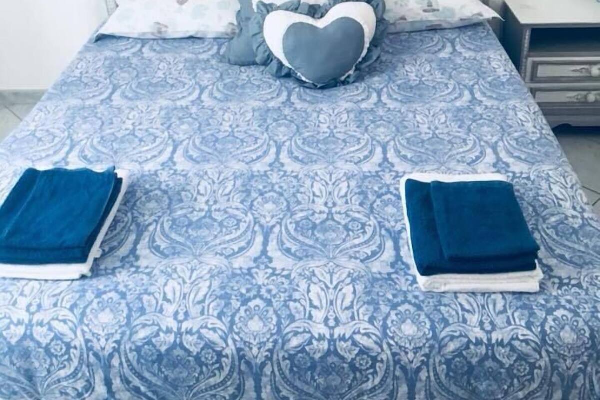 Ein ordentlich bezogenes Bett mit einem gemusterten Überwurf, herzförmigen Kissen und gefalteten Handtüchern.