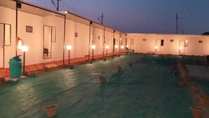 Filas de habitaciones con iluminación individual, un espacio al aire libre cubierto con piscina y un grupo de caballos al fondo.
