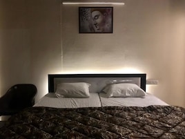 A hotel room with a bed, two pillows, a headboard, a wall-mounted artwork, and a chair.