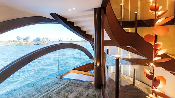 Um interior moderno com uma escadaria de vidro que dá para uma varanda com vista para a água.