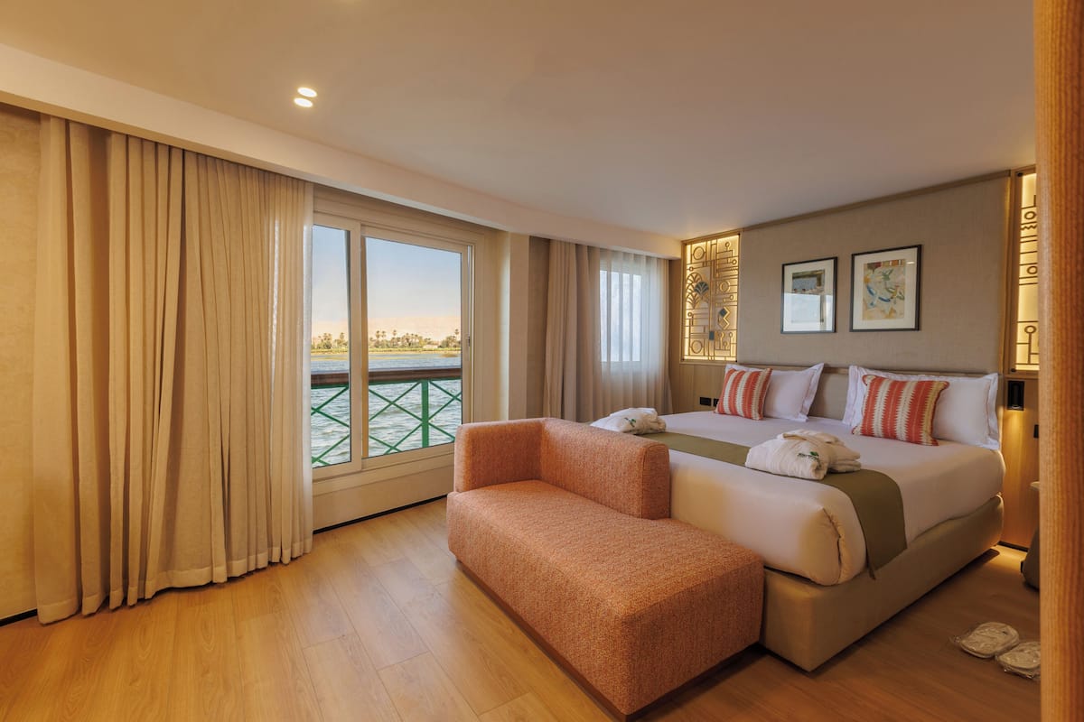 A hotel room with a large bed, a sofa, a view of the water, and a balcony.