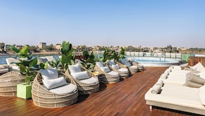 Um lounge no terraço com cadeiras de vime e um sofá, uma piscina e vista para a cidade.